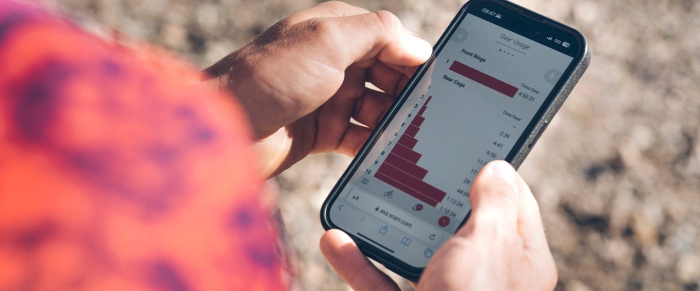 SRAM AXSのウェブサイトで自転車のギア使用状況を示す棒グラフが表示されたスマートフォンを手にしている人物。.