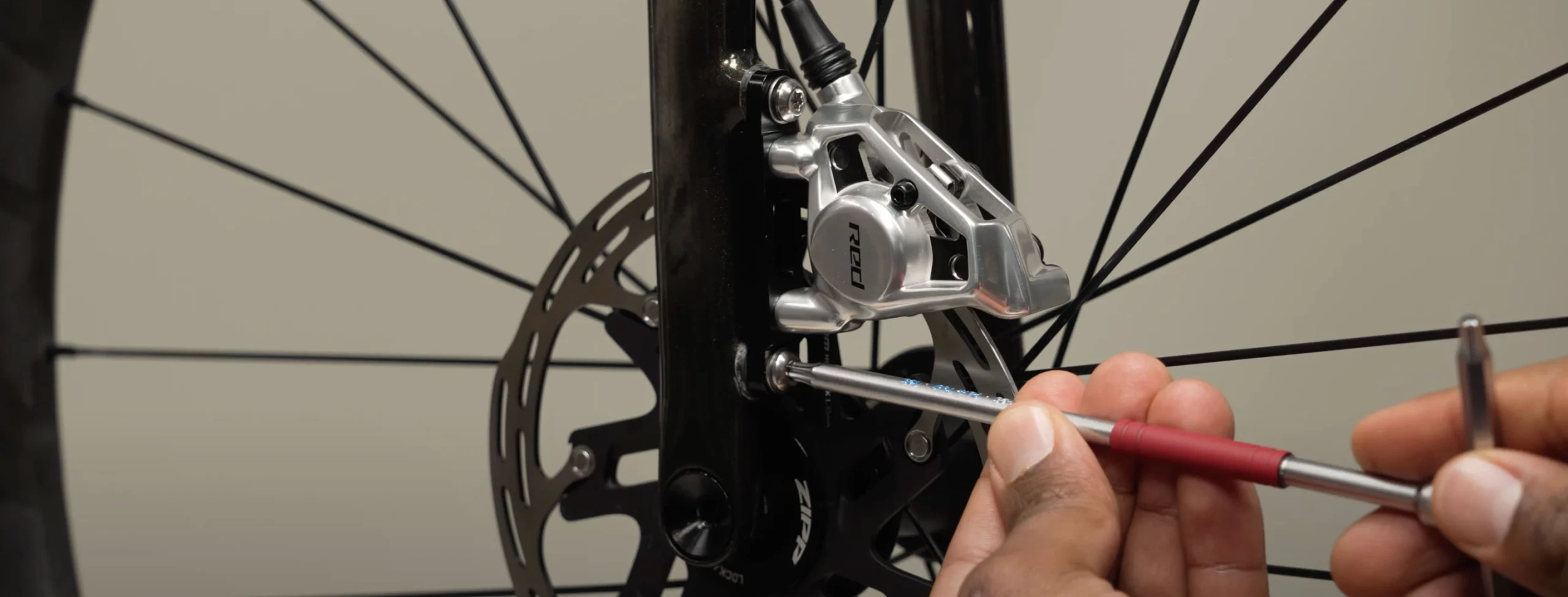 ある人が六角レンチを使って、自転車のディスクブレーキキャリパーのボルトを締め付けています。.