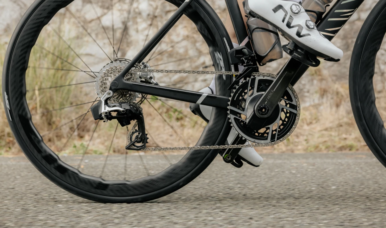 舗装道路を走行中の自転車のドライブトレインと後輪のクローズアップ。.