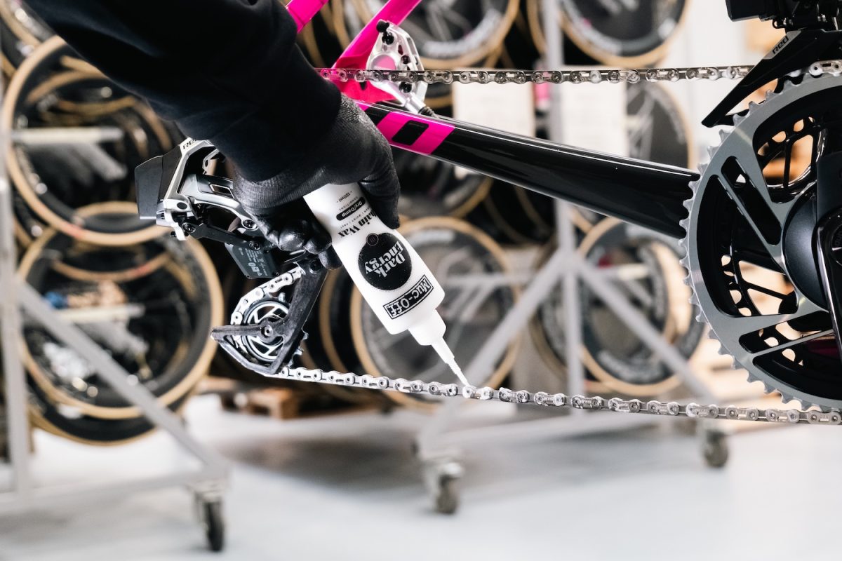 手袋をはめた手で自転車のチェーンに潤滑油を塗っている。.