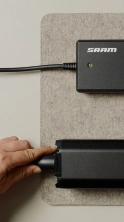 ある手が、黒いSRAMのバッテリーパックに充電ケーブルを差し込んでいる。.
