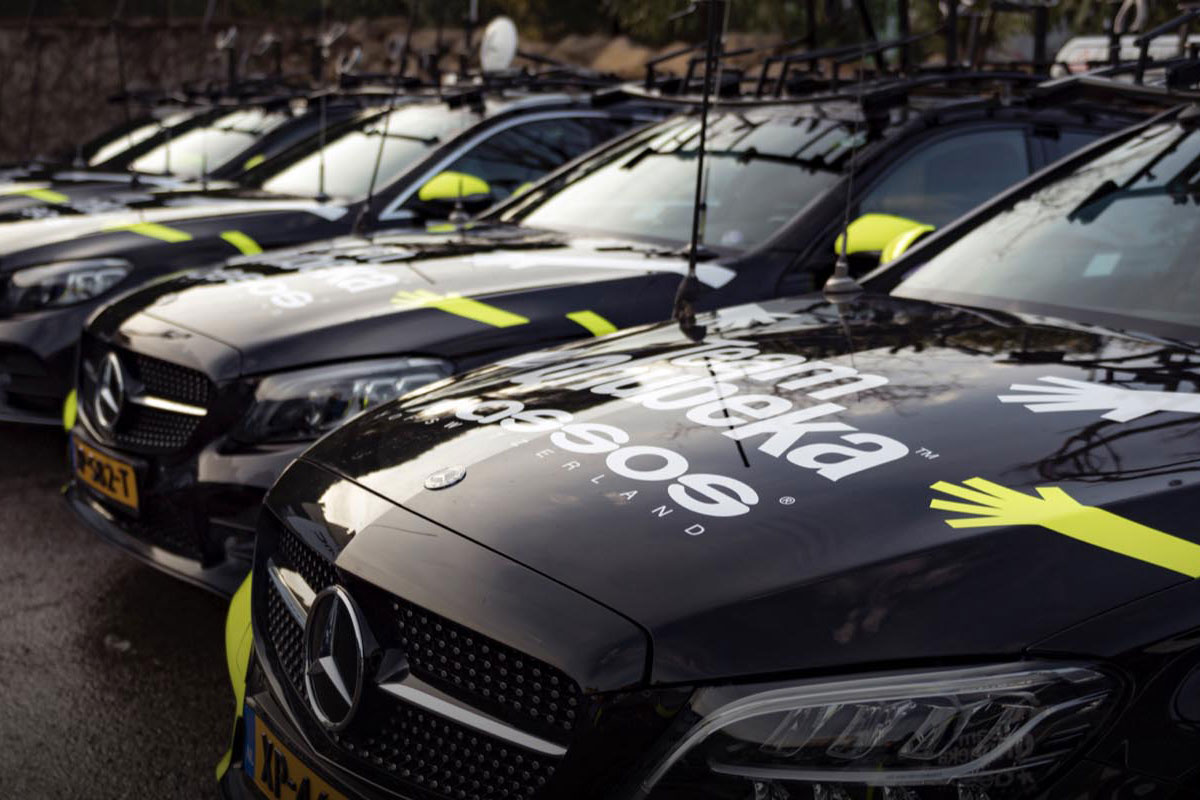 ペダルを踏むサイクリストの足のクローズアップ。自転車のギアとチェーンが見え、背景にはぼやけた紅葉がある。.