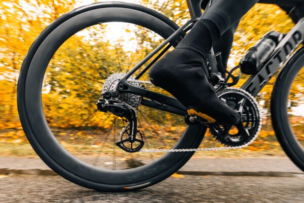 ペダルを踏むサイクリストの足のクローズアップ。自転車のギアとチェーンが見え、背景にはぼやけた紅葉がある。.