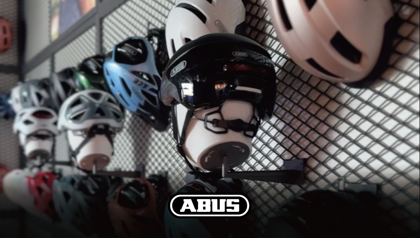壁に取り付けられたワイヤーラックに、複数のアブス製の自転車用ヘルメットが並べられている。.