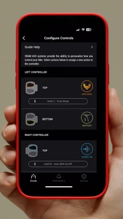 SRAM AXSアプリのConfigure Controls画面が表示されたスマートフォンを手に持つ手。この画面では、自転車用コントローラーのボタン割り当てをカスタマイズできます。.
