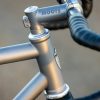 A33A0256 ROUTT製の金属製自転車フレームのクローズアップ写真。ヘッドチューブ、ステム、そしてグリップが巻かれたハンドルバーが見える。.
