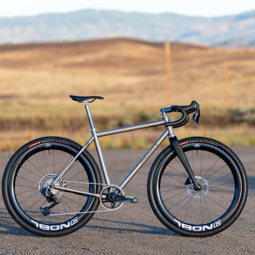 カーボンホイールとドロップハンドルを備えたチタン製のROUTT製グラベルバイクが、舗装道路に停められている。.