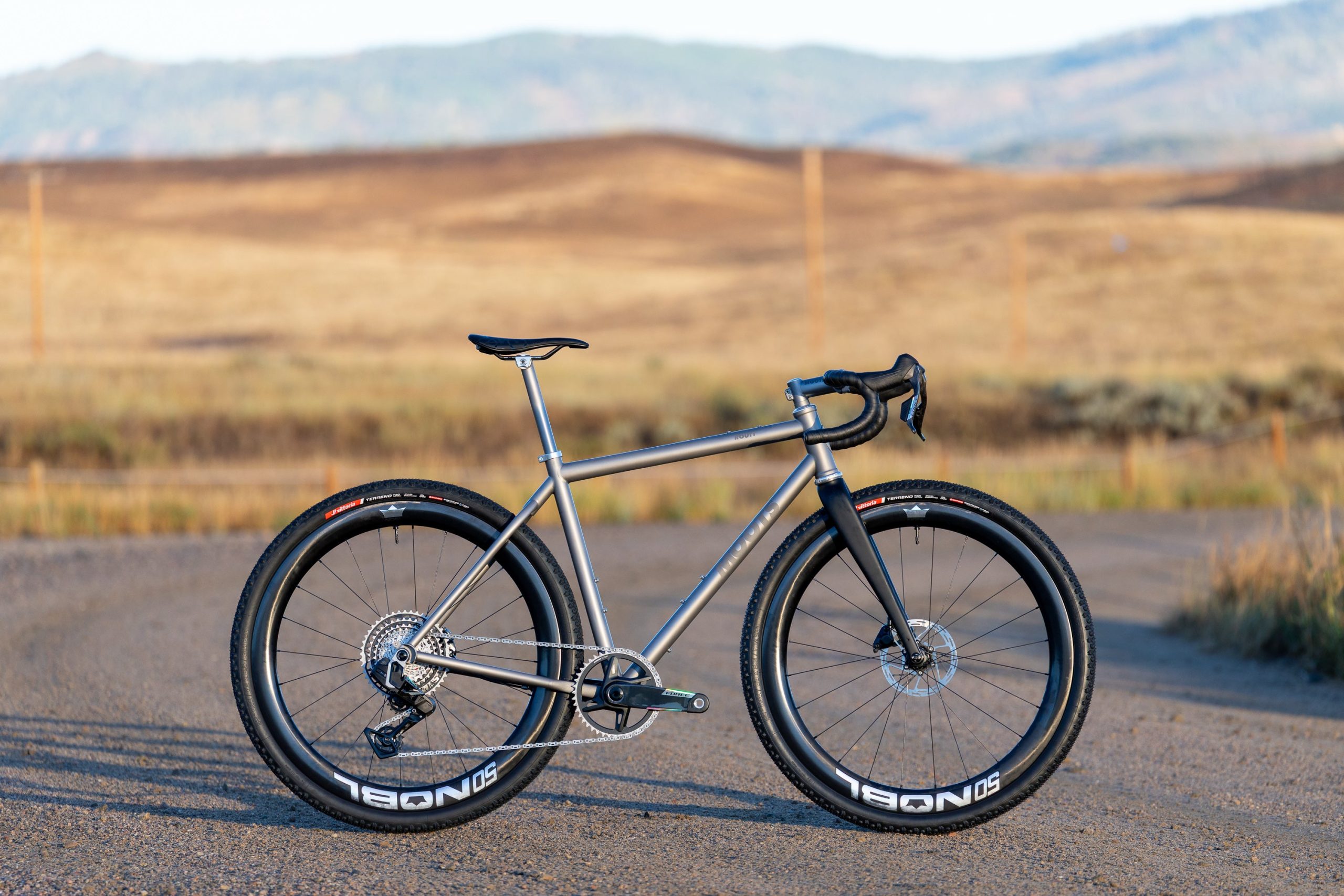A33A0269 カーボンホイールとドロップハンドルを備えたチタン製のROUTT製グラベルバイクが、舗装道路に停められている。.