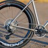 A33A0271 ROUTT製のチタン製グラベルバイクフレームのクローズアップ。シングルチェーンリングのドライブトレイン、リアディレイラー、そしてノッビータイヤを装着したディープセクションのカーボンホイールが特徴だ。.
