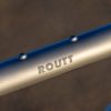 A33A0277 側面にROUTTと刻印された、灰色の自転車フレームのチューブのクローズアップ。.