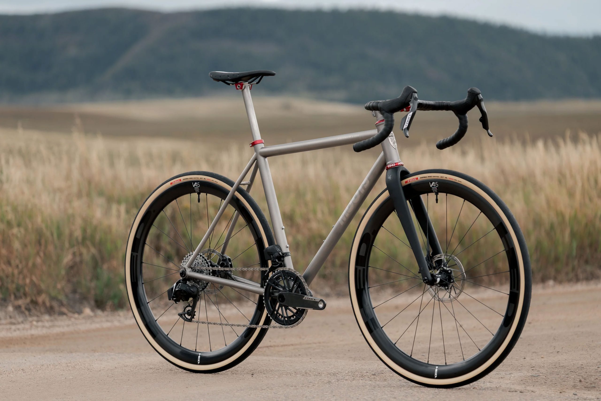 A33A1650 グレーのメタルフレーム、ドロップハンドル、ディープセクションのカーボンホイールを備えたCOUNTY LINE ALL-ROAD BIKEが、未舗装の道に停まっている。.