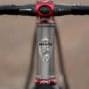 A33A1654 COUNTY LINE ALL-ROAD BIKEのヘッドチューブのクローズアップ。自転車に乗った山岳恐竜の盾型のロゴが施されており、ハンドルバーとフォークには赤いパーツが採用されている。.