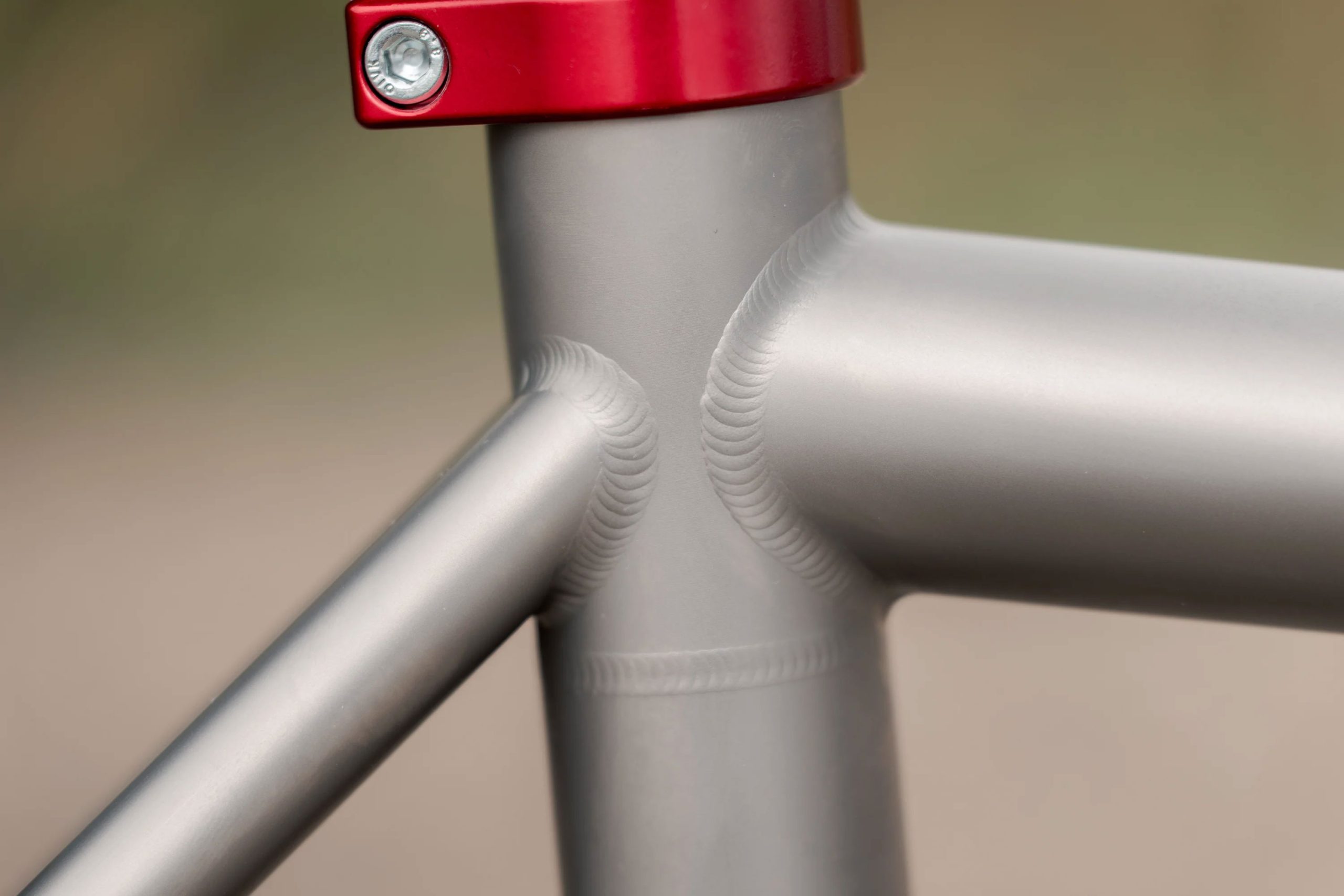 A33A1682 COUNTY LINE ALL-ROAD BIKEのマットグレーのフレーム接合部のクローズアップ。金属の溶接跡が際立ち、赤いシートポストクランプが特徴的です。.