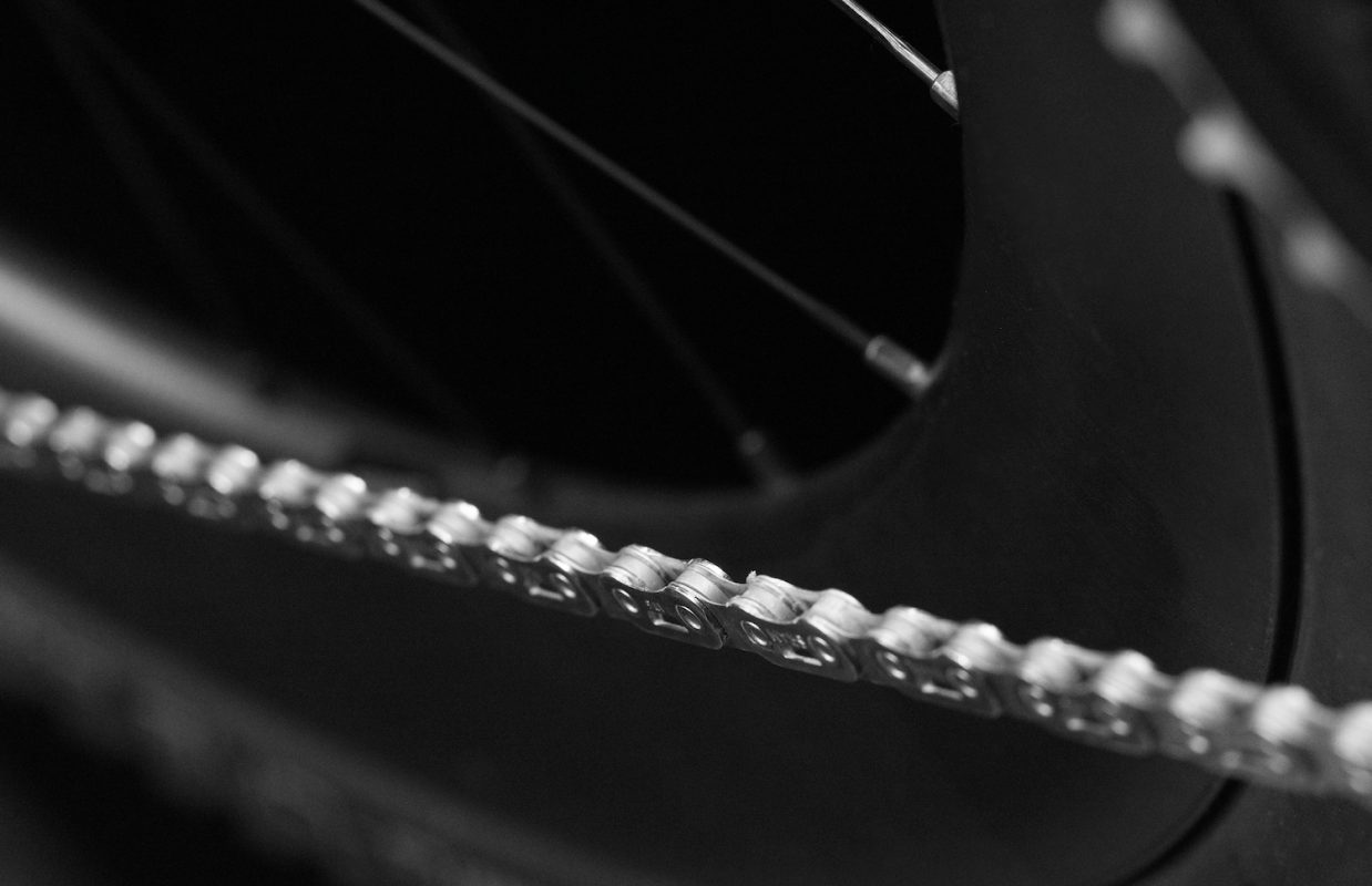 自転車のチェーンと後輪のクローズアップ。黒いタイヤとスポークを背景に、チェーンのリンクがシャープに写っている。.
