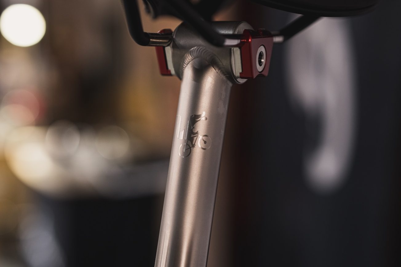 サドル取り付け部の近くに、自転車に乗った小さな動物のロゴが刻印された自転車用シートポストのクローズアップ。.