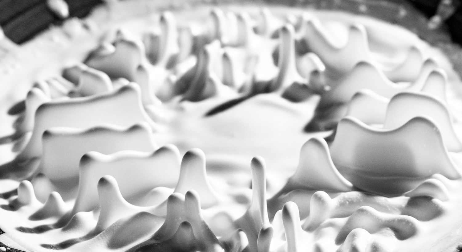 ミルクかクリームと思われる、白い液体が尖った形になって上に飛び散る様子をハイスピード撮影（モノクロ）で捉えたクローズアップ。.