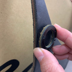 黒い革のストラップに取り付けられた金属製のグロメットを、指で握っている。.