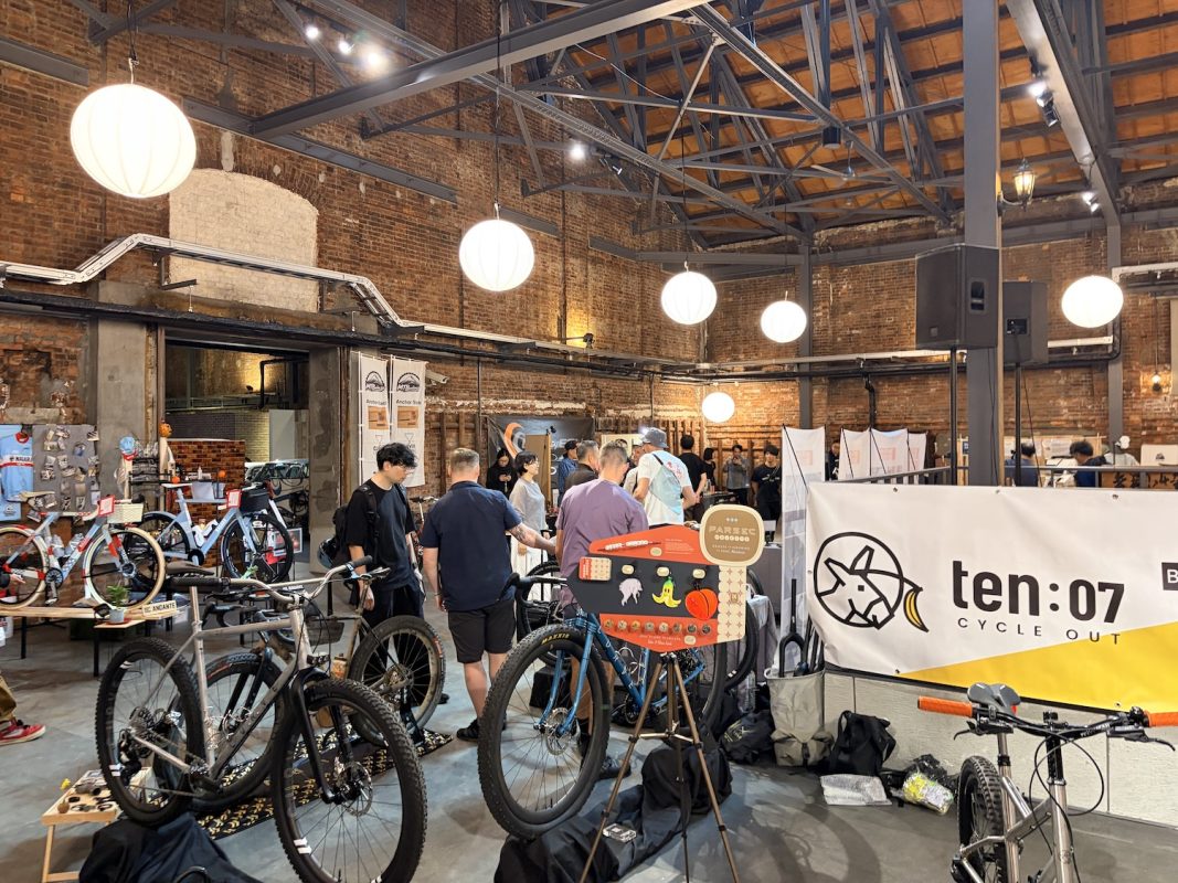 Ten:07 cycle outのバナーが掲げられた屋内見本市で、自転車を物色する人々。.