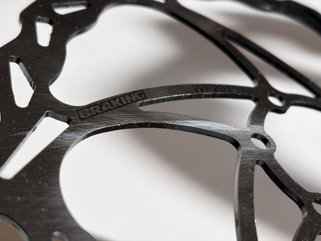 表面にブランド名BRAKINGと型番が刻印された、黒い金属製の自転車用ブレーキローターのクローズアップ写真。.