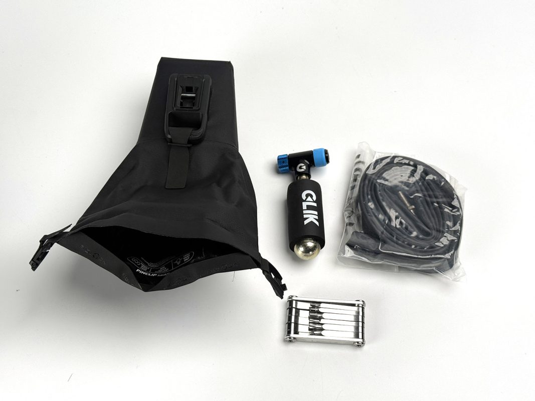 黒いサドルバッグ、CO2インフレーター、ビニール袋に入った巻き取り式のチューブ、そしてマルチツール。.