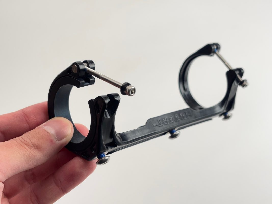 無地の背景に、2つの円形の開口部と接続ネジのある黒い金属製のクランプを持つ手。.