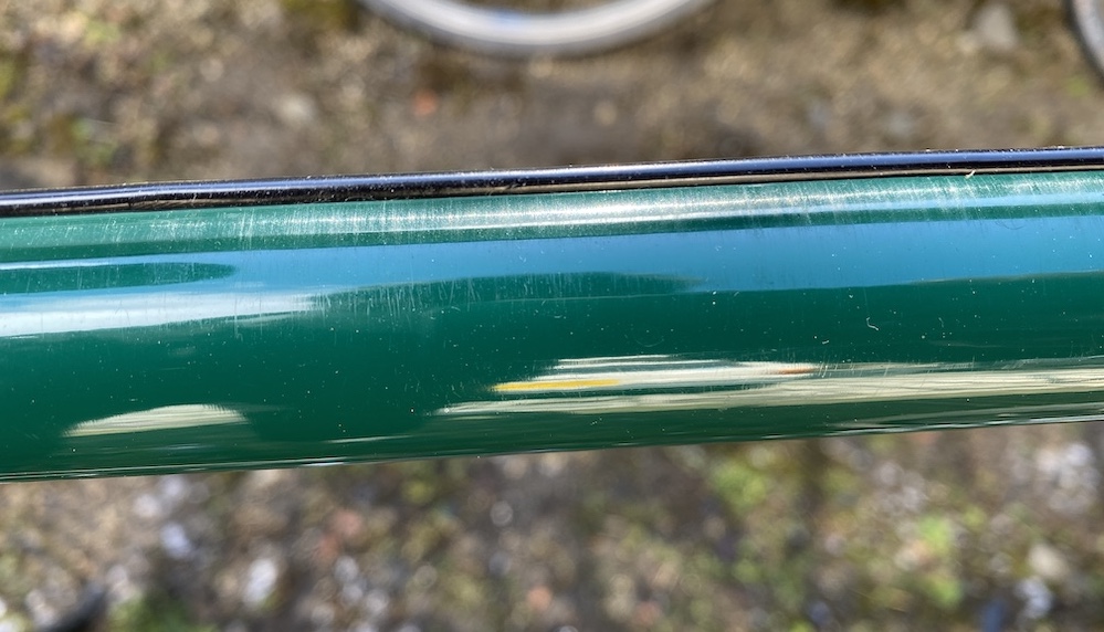 表面に傷が見える、濃い緑色の自転車のフレームチューブのクローズアップ。.
