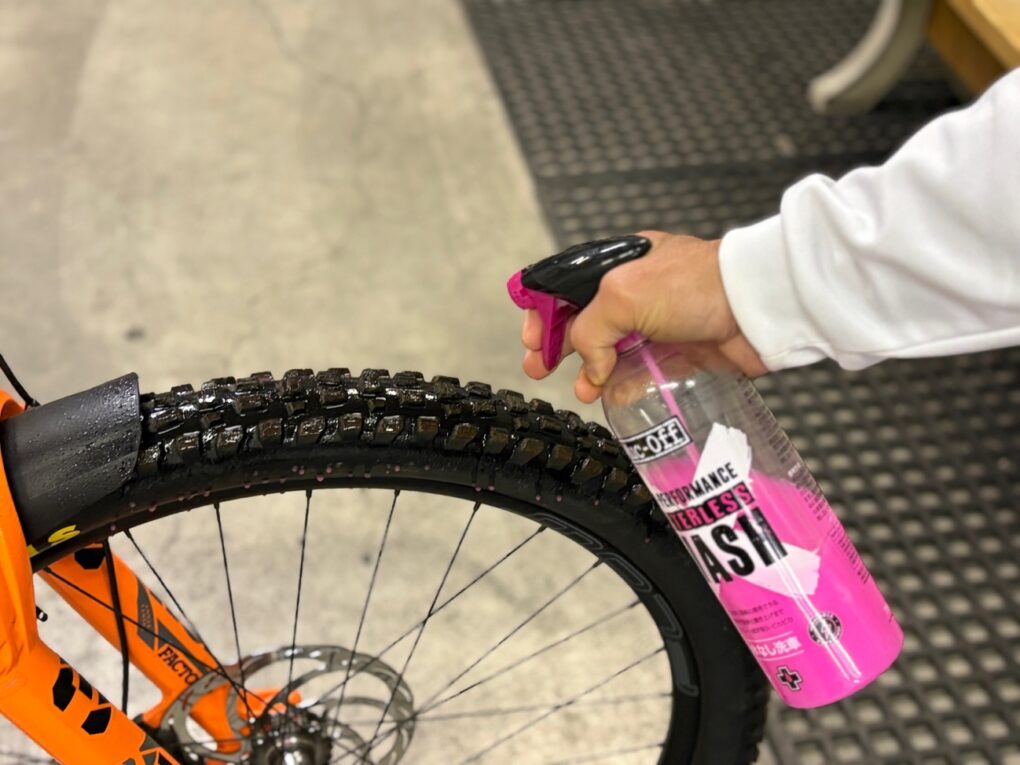自転車タイヤに、ピンクのMuc-Off水なし洗浄剤を手でスプレーしている様子。.