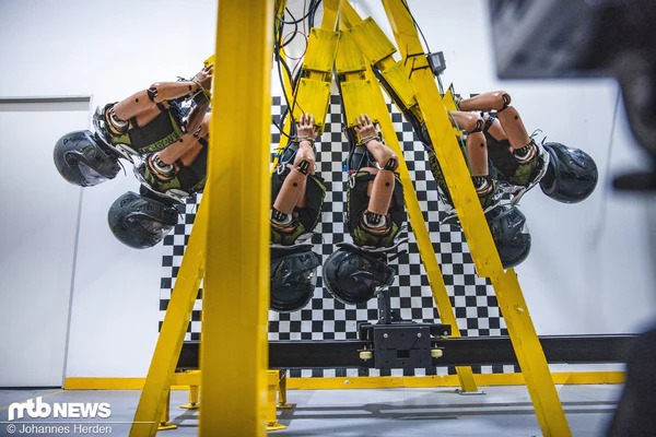 黄色いフレームに取り付けられたテスト用ダミーのヘルメット振り宣裝置の写真