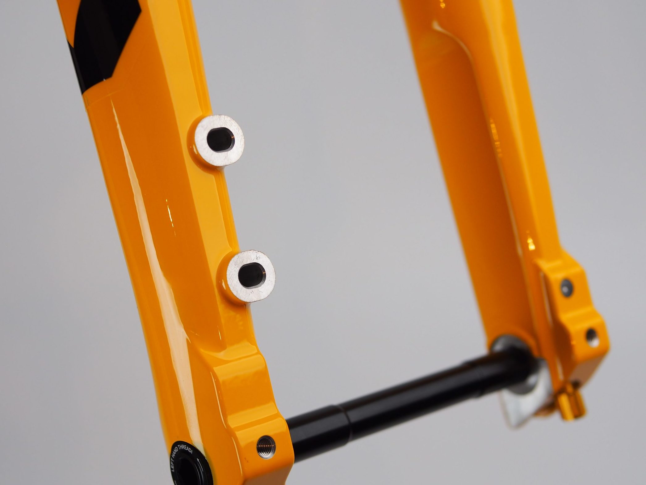 2つのマウントボスと黒いスルーアクスルを備えた、鮮やかな黄色の自転車用フォーク。.