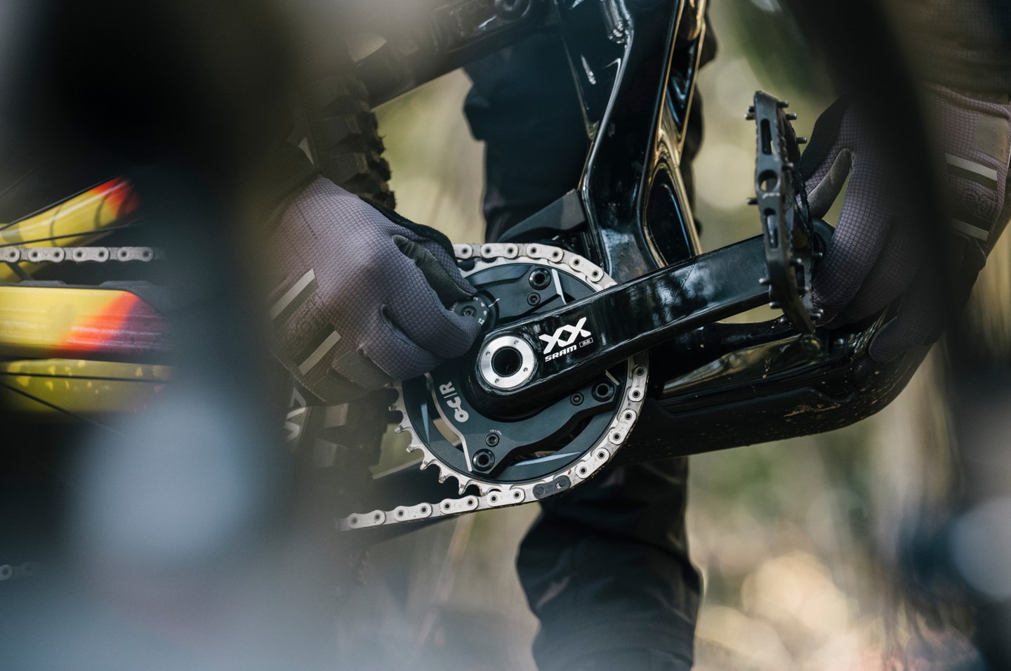 マウンテンバイクのクランクセットを調整する、手袋をはめた手のクローズアップ。.