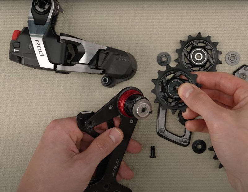プーリーホイール付きのSRAM Red XPLR自転車用リアディレイラーケージを組み立てている手。.
