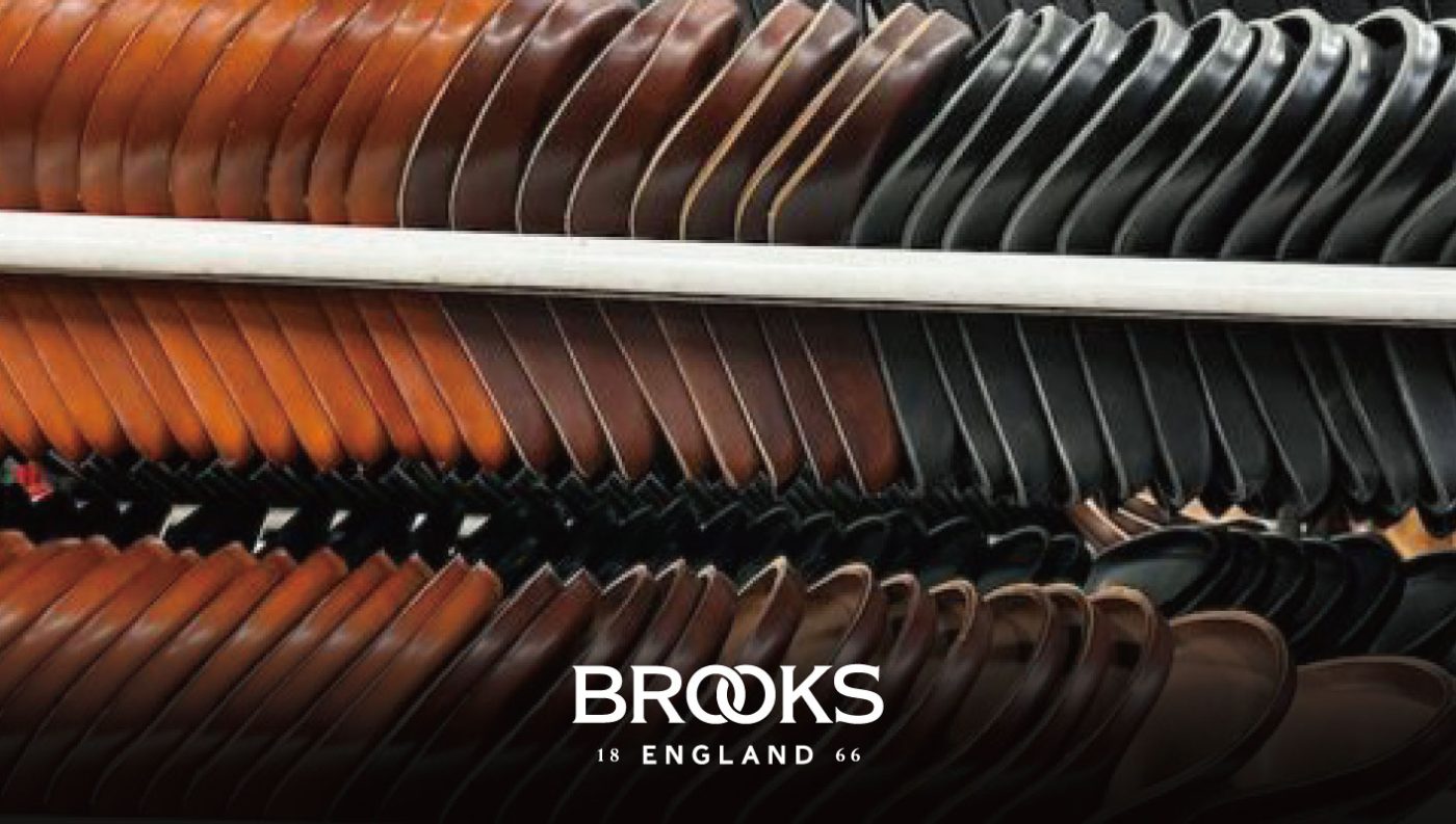 陳列ラックに並んだ茶色と黒色のレザー製自転車サドル。下部にはBrooks Englandのロゴが入っている。.