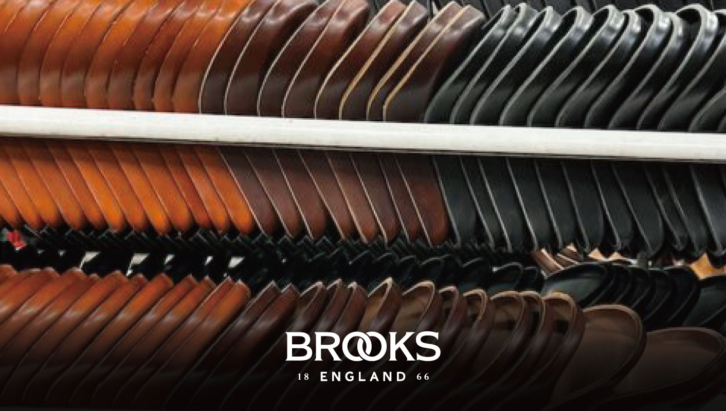 陳列ラックに並んだ茶色と黒色のレザー製自転車サドル。下部にはBrooks Englandのロゴが入っている。.