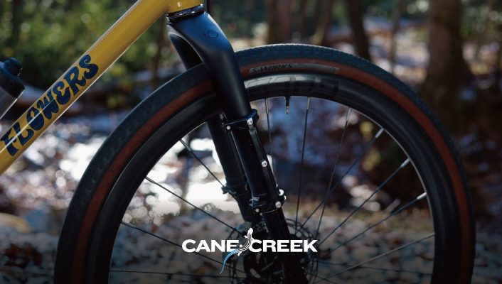 FLOWERSの文字が入った黄色い自転車の前輪とフォークのクローズアップ。.