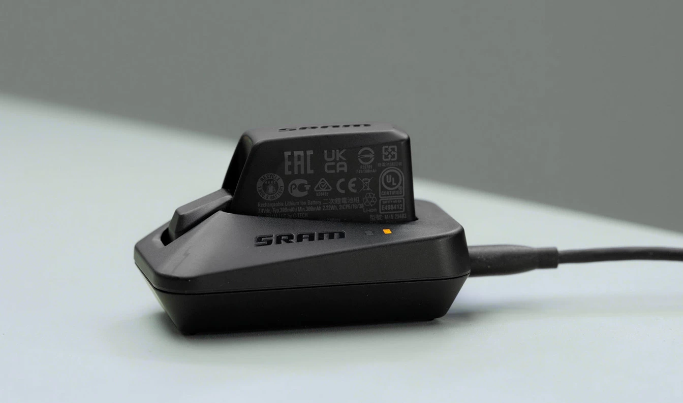 電源ケーブルが接続された状態で、ベースにセットされ充電中の黒いSRAMバッテリー。.