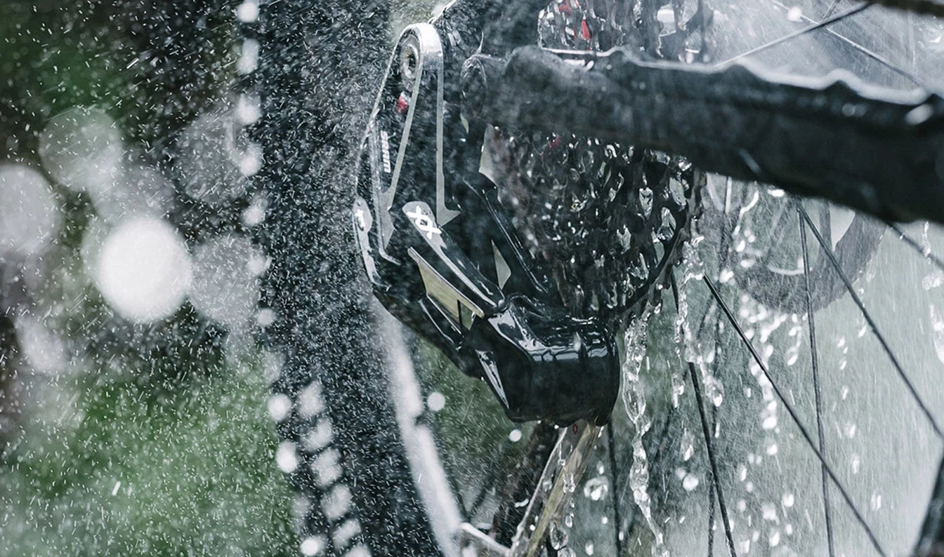 自転車用ディレイラーとカセットに水が吹きかけられている様子のクローズアップ。.
