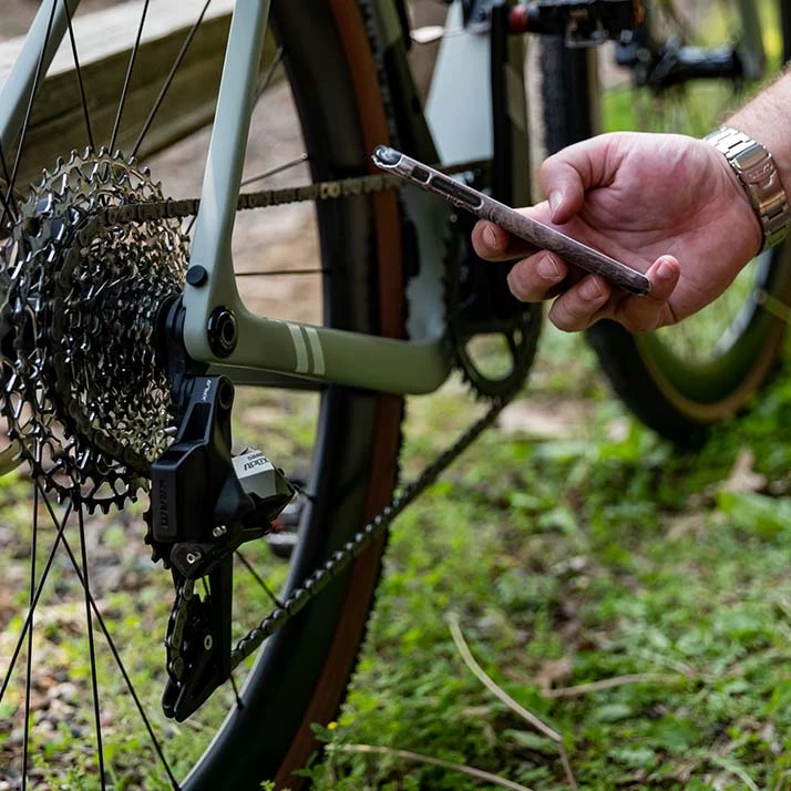 自転車のリアディレイラーとカセットの近くにスマートフォンを構えている人。.