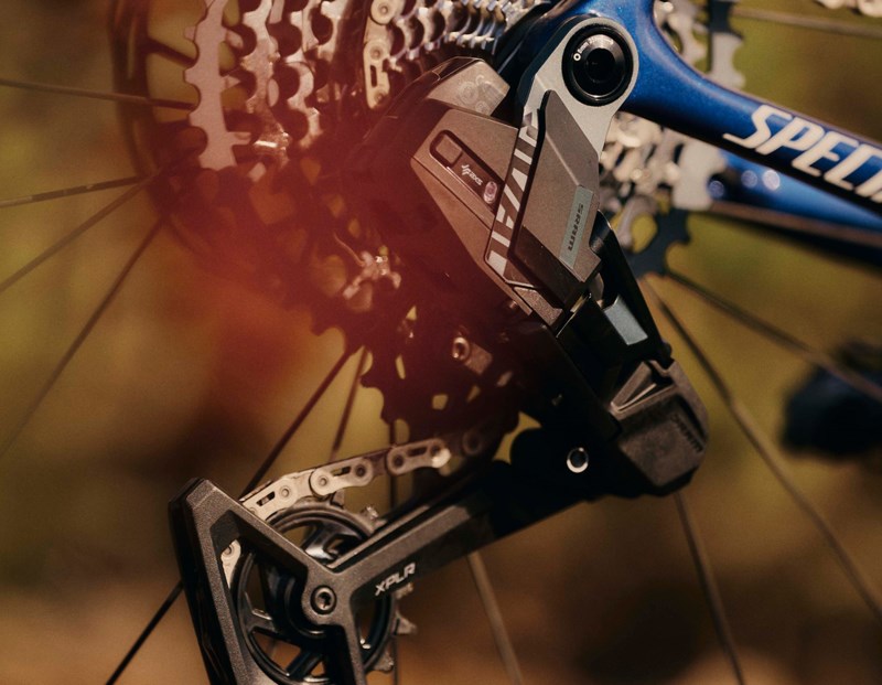 青いスペシャライズドの自転車フレームに装着された、SRAM Rival XPLRのリアディレイラーとカセットのクローズアップ写真。.