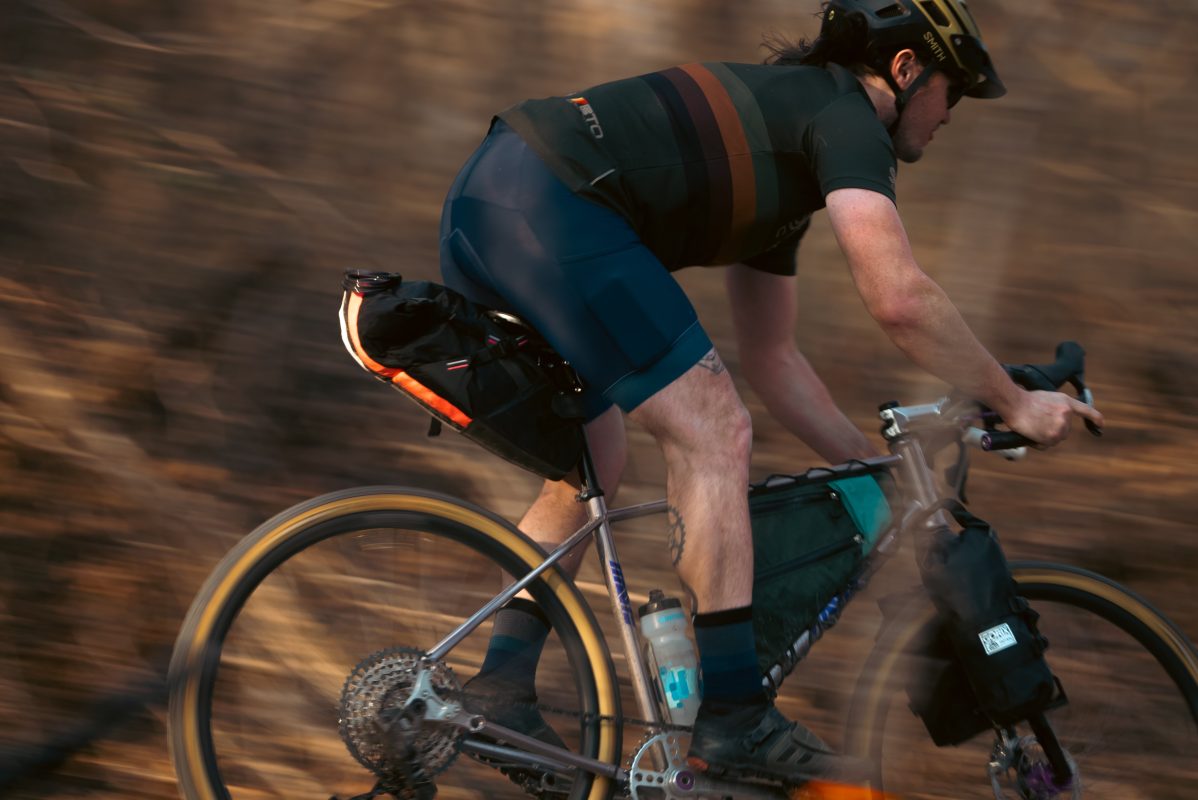 ヘルメットをかぶり、サイクリング用具を身に着けたサイクリストが、未舗装の道を満員の自転車で走っている。.