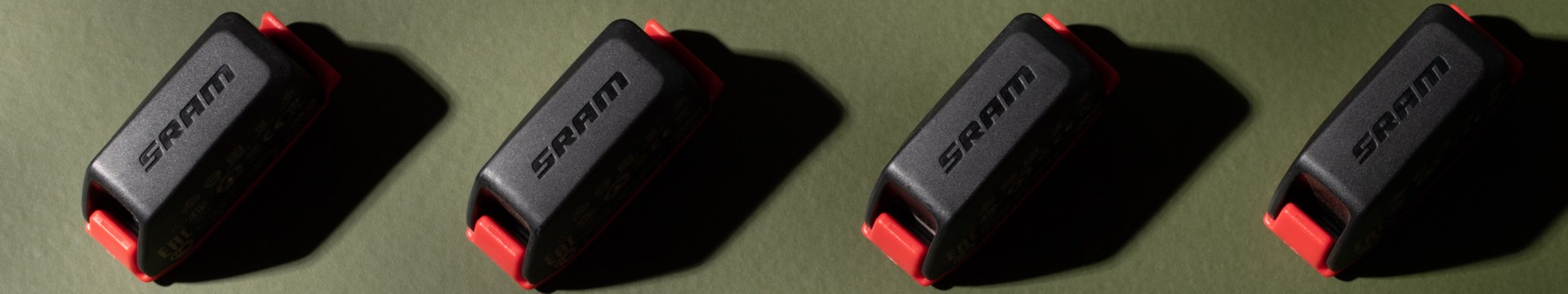 緑色の背景を背に、4つのSRAM製電子シフト用バッテリーが一列に並べられている。.