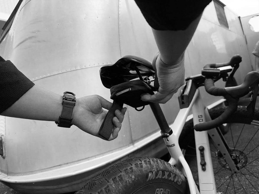 自転車のサドルの下側に、小さなファスナー付きのポーチを取り付けている人。.