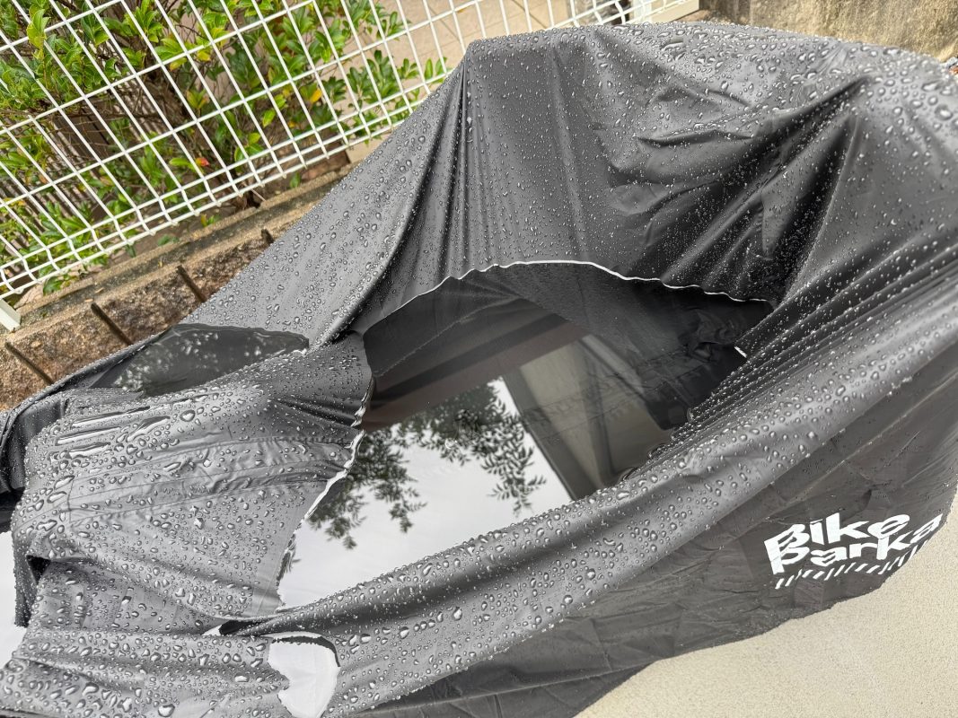 雨に濡れた黒いバイクパーカーの表面に、雨水がたまっている。.
