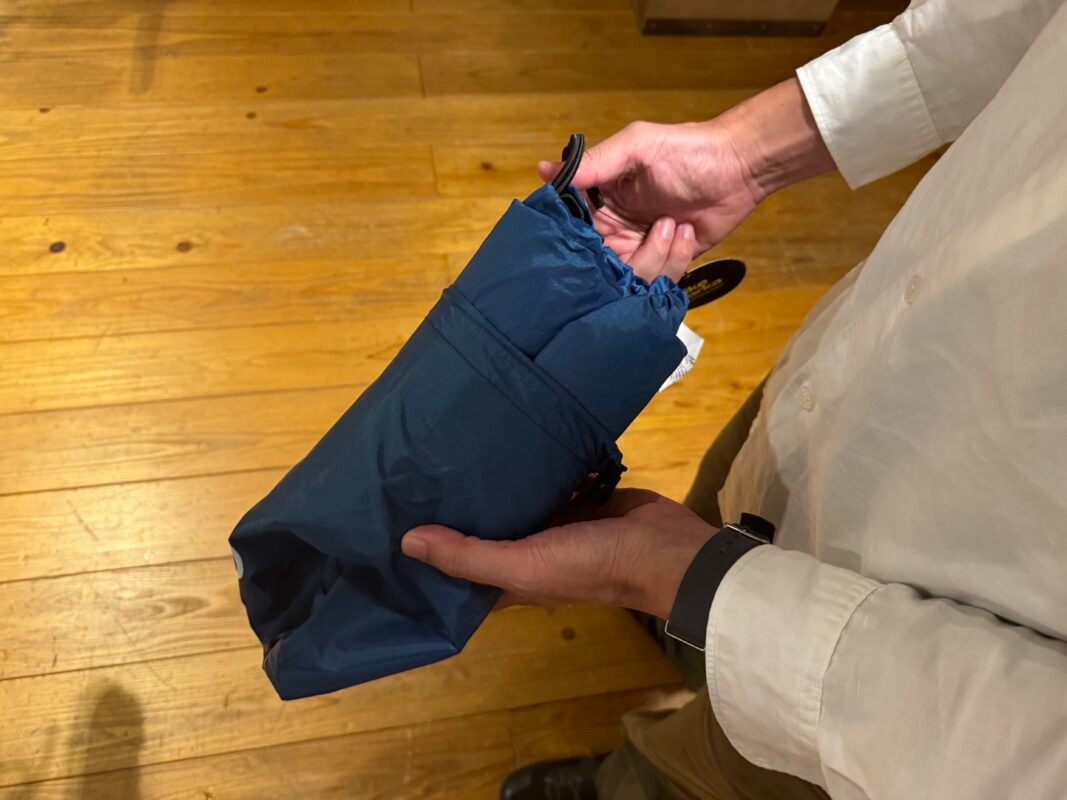 ひもで開閉する、折りたたまれた青い布製のポーチを両手で持っている。.