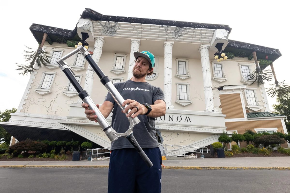 逆さまになった建物の前で、自転車のサスペンションフォークを手に持っている男性。.