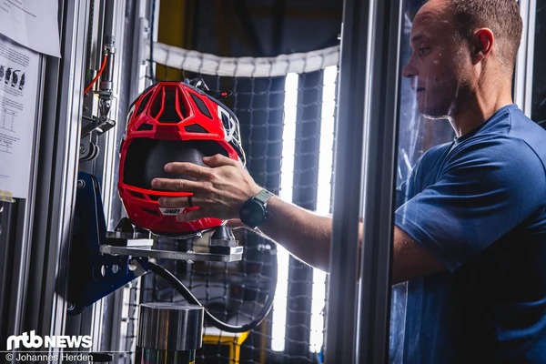 赤いヘルメットをテスト裝置にセットする人物の写真