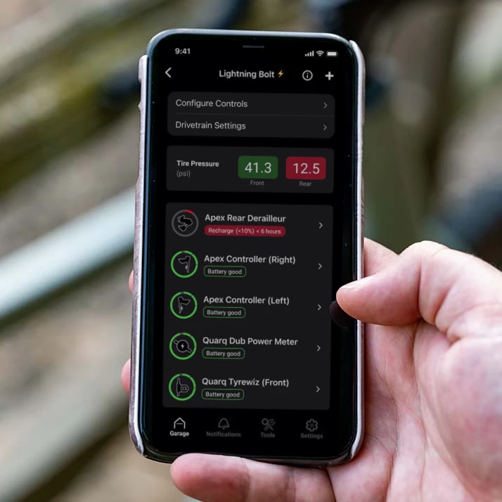 Lightning Boltアプリのインターフェースが表示されたスマートフォンを手に持つ手。画面には、自転車の部品のバッテリー残量とタイヤの空気圧が表示されている。.