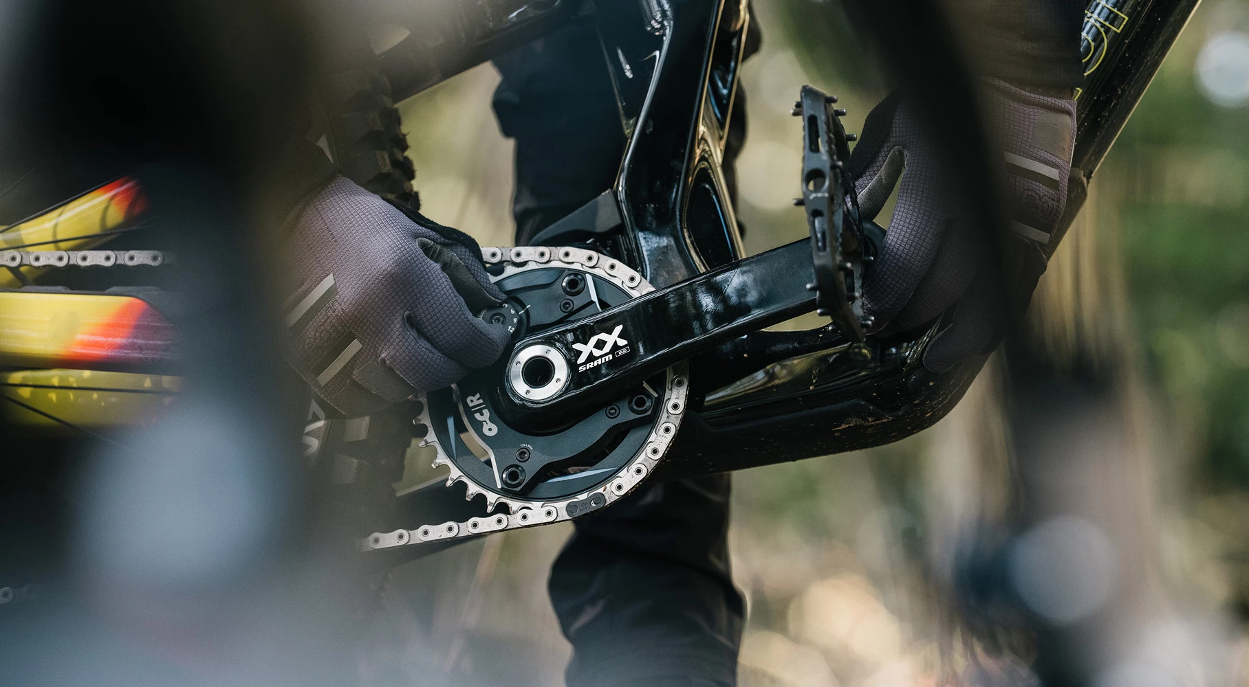 手袋をはめた人が、マウンテンバイクのSRAM XXクランクセットとチェーンリングを調整している。.