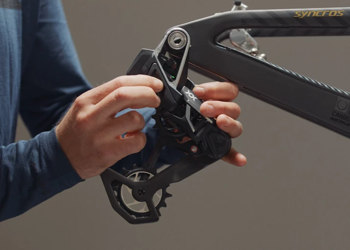 自転車のフレームで、リアディレイラーを調整している人の手。.