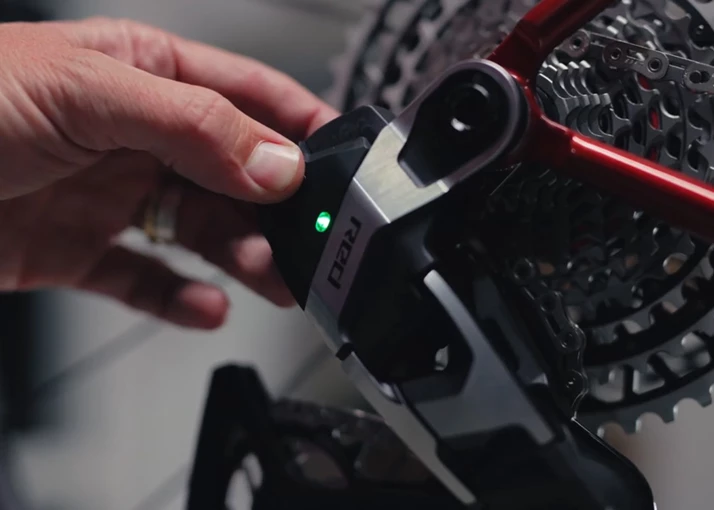 SRAM Redの自転車用リアディレイラーのボタンを押している指。そのボタンには、小さな緑色のライトが点灯している。.