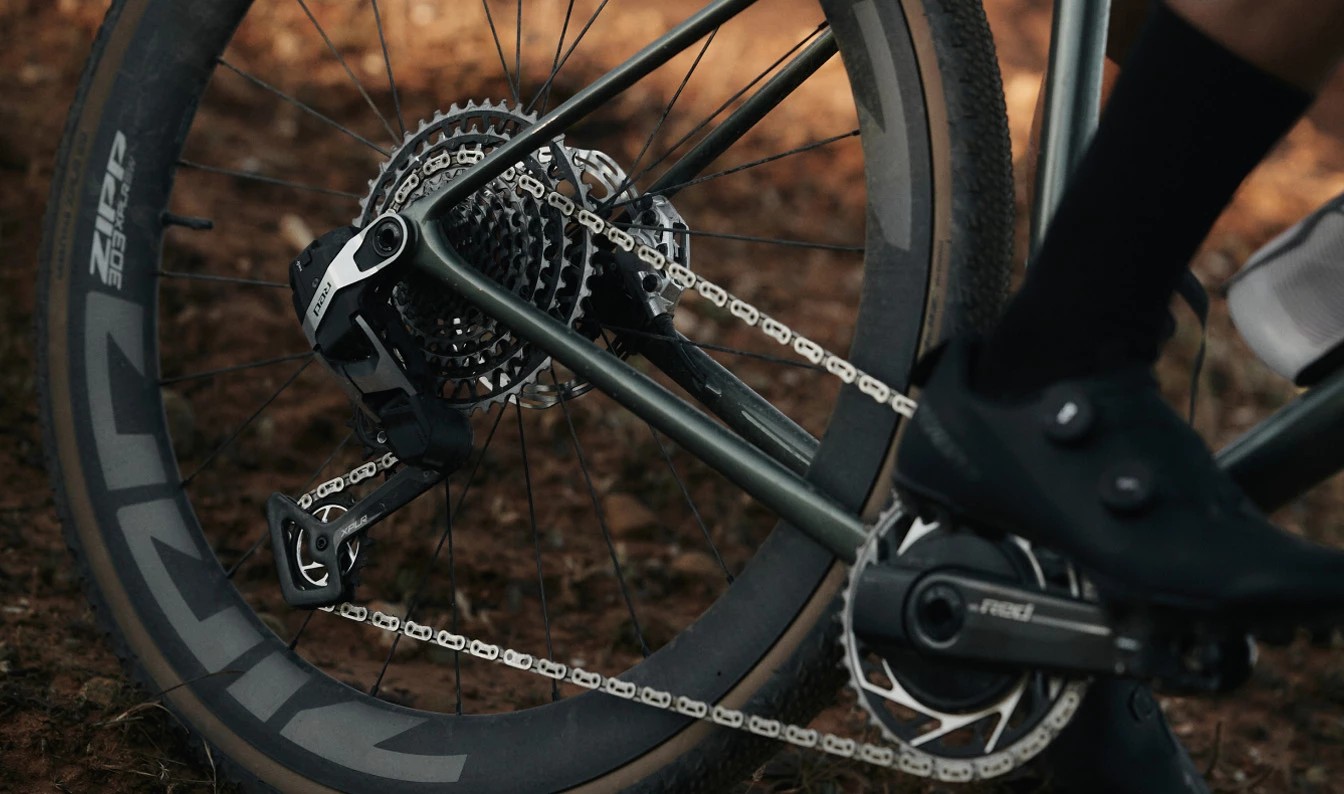 SRAM Redのディレイラー、カセット、クランクセットを備えた自転車のドライブトレインのクローズアップ。ペダルにはサイクリングシューズが乗っている。.